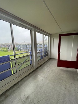 A balcony with large windows and a red door, offering views of the exterior.
