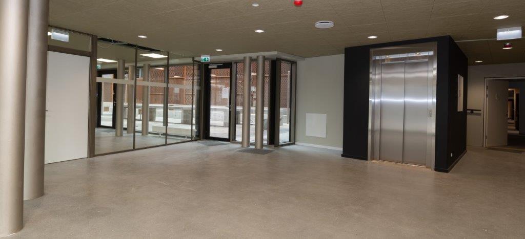 Interior view of a building lobby with an elevator and glass entrance doors.