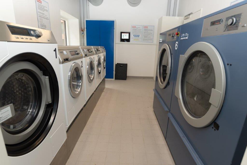 A row of washing machines and dryers in a communal laundry room.
