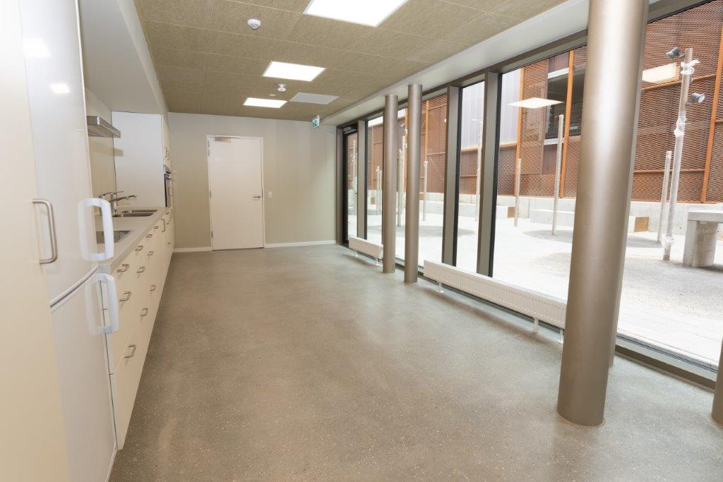 A long, empty common room or kitchen area with large windows overlooking an outdoor space.