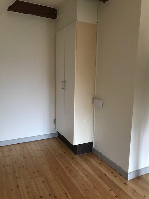 A built-in white wardrobe or storage unit in a room with light wooden flooring and a sloped ceiling.