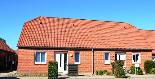 Front view of a red brick building with a tiled roof, multiple windows, and white doors, under a clear blue sky.