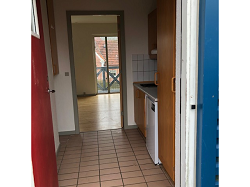 View from the entrance hallway showing a compact kitchen area with a dishwasher and an open doorway leading to a living space with a balcony.