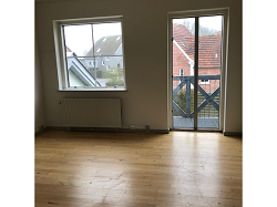 Empty living room with light wooden flooring, a large window, and a glass door leading to a balcony.
