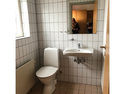 Bathroom with white tiled walls, a toilet, a wall-mounted sink, and a mirror above the sink.