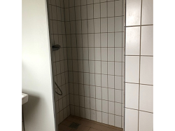 Tiled shower area with a shower head and a drain on the floor, located within a bathroom.
