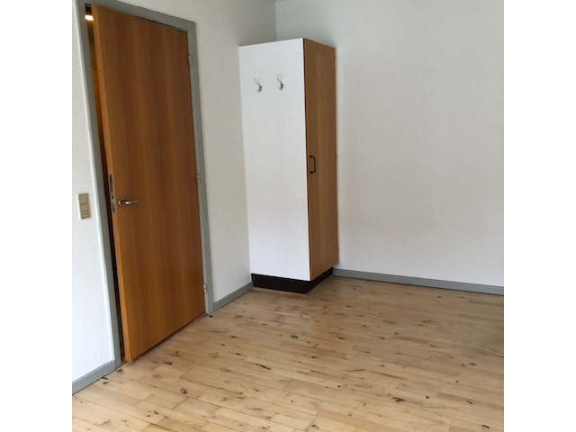 Seomra le hurlár adhmaid éadrom, doras adhmaid atá oscailte go páirteach, agus comh-aireachta ard bán agus adhmaid le crúcaí cótaí.