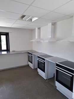 A kitchen area with multiple built-in ovens, stainless steel countertops, and white extractor hoods.