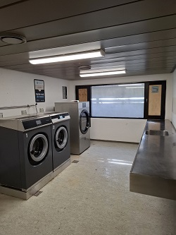 A laundry room with several industrial washing machines, a dryer, and a stainless steel countertop with a sink.