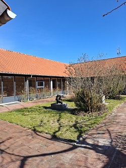 Exterior view of a building with a red tile roof, glass facade, and a grassy courtyard with a small sculpture.