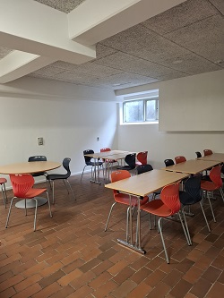 Dining or break room with various tables and chairs, featuring a brick-patterned floor and a window.