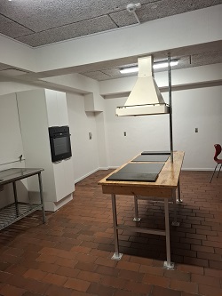 Erhvervskøkken med central ø-kogestation i træ, indbygget ovn og stor emhætte.