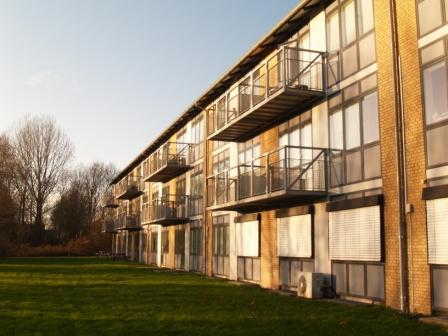 Exterior view of a modern apartment building with balconies and large windows, seen from a grassy lawn.