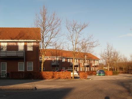 Välisvaade punaste kivikatuste ja paljaste puudega tellistest kortermajadele, mille esiplaanil on parkla.